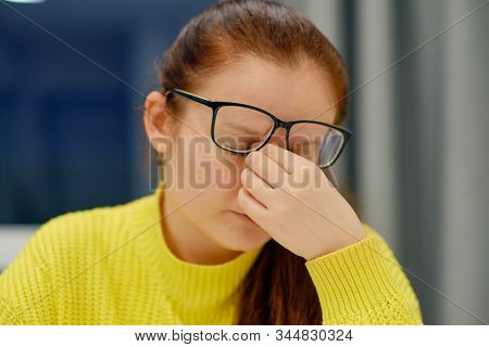 Young Caucasian Female In Glasses And Knitted Sweater Doing The Nose Massage When Reading Electronic