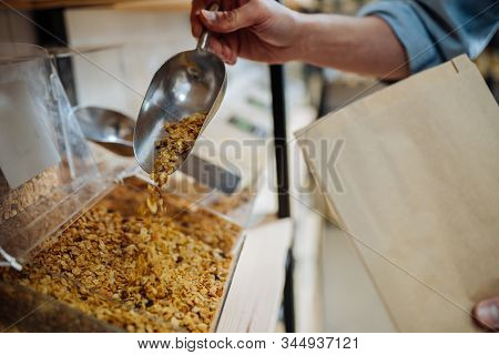 Close Up Of Hands Unrecognizable Male Worker Shop Assistant Filling Paper Bag With Oat Granola In Bu