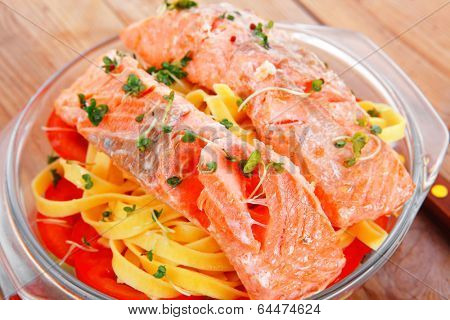 fresh fried natural pink salmon on italian traditional tagliatelle backed with tomato and vegetables served over wooden table with cutlery
