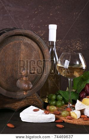 Supper consisting of Camembert cheese, wine and grapes on cutting board and wine barrel on wooden table on brown background