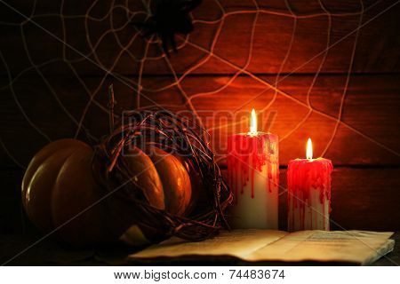 Halloween decoration with spider on web, book, pumpkin and candles on wooden background