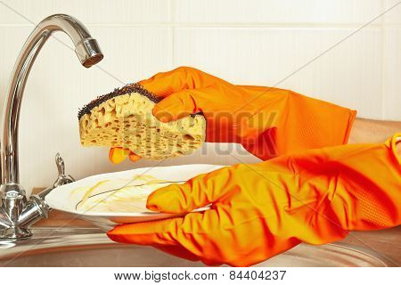 Hands in gloves with sponge and dirty saucer over the sink in kitchen