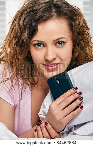Radiant woman with phone lying on bed