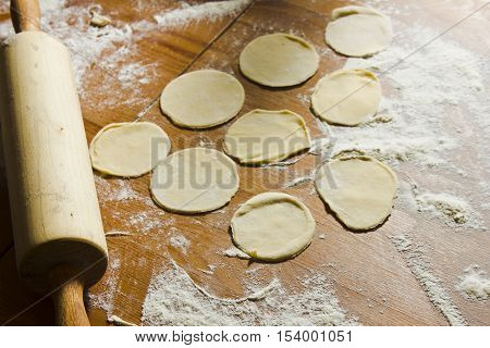 Circles of dough and rolling pin on the wooden table. Homemade process of preparation Russian Belarussian Ukrainian meals 