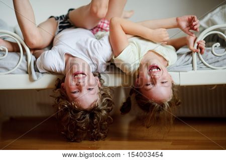 The children boy and girl naughty on the bed in the bedroom. They lie side by side their heads hanging off the bed. Children is very amused.
