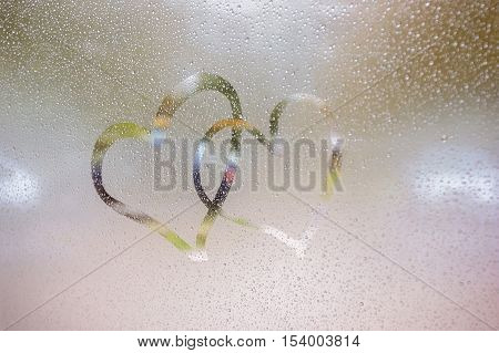 Two hearts drawn on a wet window glass. Rainy autumn