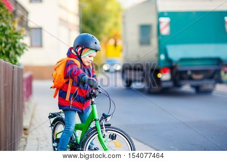 Lovely preschool kid boy in helmet riding with his green bike in the city. Happy child in colorful clothes biking on way to nursery. Active leisure for kids outdoors with bicycle.