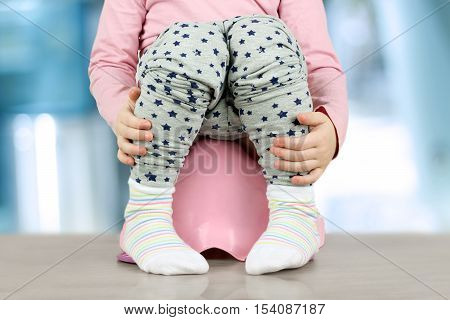 Children's legs hanging down from a chamber-pot on a blue background