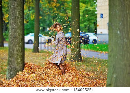 Cute attractive girl whirls and throws leaves in the air on the walk around the house a clear autumn day.