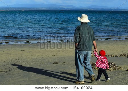 Grandfather with granddaughter walks on the beach during winter.