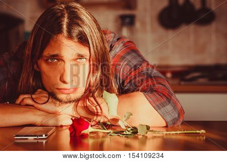 Disappointment and depression. Unrequited love concept. Young worried disappointed man with single red rose and smartphone mobile phone waiting for his girlfriend.