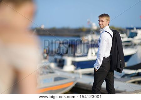 Handsome groom's portrait at small harbor on summer day
