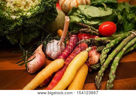 A variety of different colored carrots fresh from and organic garden with Cabbage gourds asparagus tomatoes rosemary herb shallots and garlic on a wooden cutting board