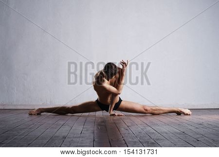 Handsome ballet dancer sitting on a splits. Warm up on the floor.