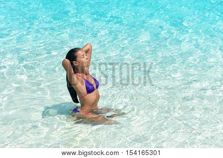 Beach sexy woman in bikini swimming in perfect crystalline blue water ocean. Beautiful Asian girl sun tanning and relaxing in tropical sea taking care of her hair and skin.