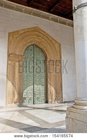 The bronze Romanesque door of Monreale Cathedral with the carved stone door frame decorated with mosaic patterns Sicily Italy.