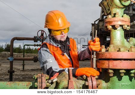 Woman engineer in the oilfield repairing wellhead with the wrench wearing orange helmet and work clothes. Oil and gas concept.