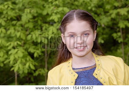 Humeral portrait of smiling girl in yellow jacket in green park.