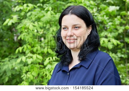 Humeral portrait of dark-haired smiling woman in green summer park.