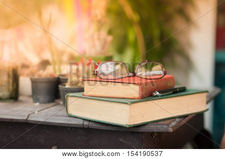 Glasses with books and pen on wood table in morning time. weekend lifestyle concept. focus on red vintage book spine