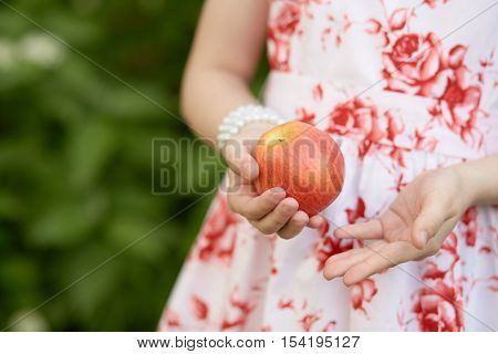 Hands of girl in flowery dress holding red apple outdoor.
