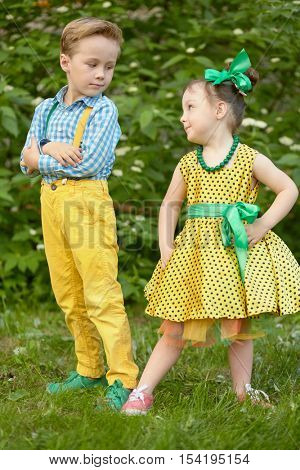 Little boy and girl stand at grassy lawn looking at each other.