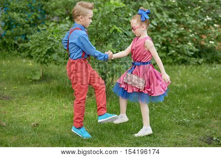 Boy and girl dressed in red and blue costumes dance at grassy lawn.