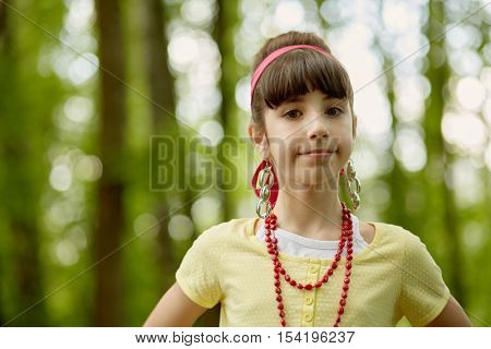 Portrait of girl with red necklace, earrings and red headband standing in summer park.