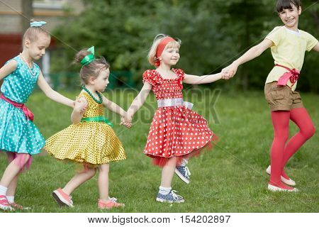 Four girls dance holding hands at grassy lawn.