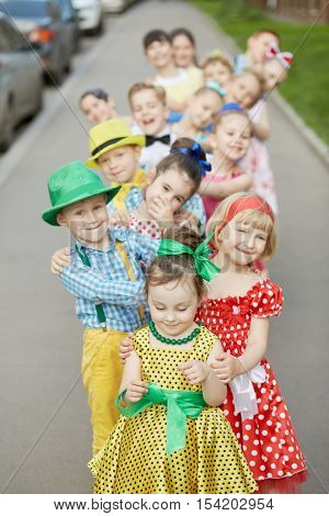 Fifteen children stand one by one bending to defferent sides at sidewalk, focus on first girl.
