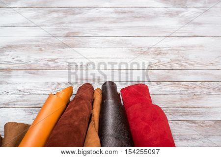 Brightly colored leather in rolls on the white wooden background. Leather craft. Copy space.