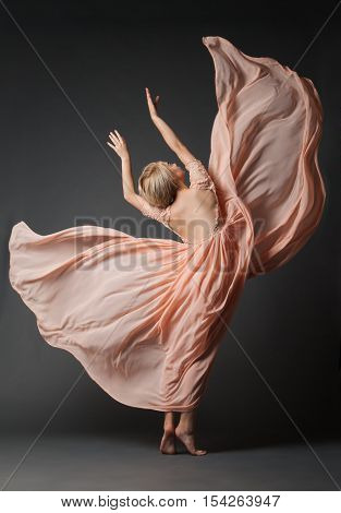 Young woman in light chiffon dress dancing on black plain .