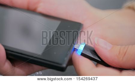 Woman's hand plugging black lightning charging cable into smartphone - USB data cable connecting on modern gadget. Close up