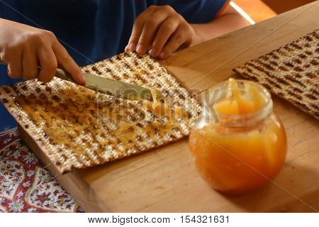 Jewish child hands spread honey on Matzo bread during Passover Jewish holiday.