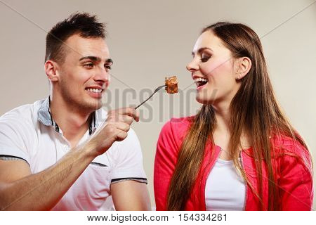 Smiling man feeding happy woman with cake. Wife and husband eating caloric food.