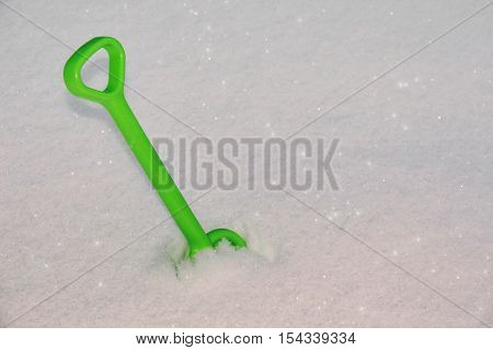 White snow background sparkling in sun and green children's shovel stucking in snow. Shallow depth of field focus on shovel