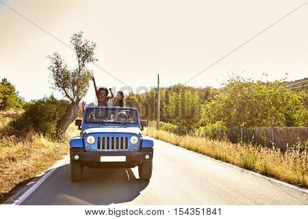 Four friends on the road in open car, two women standing