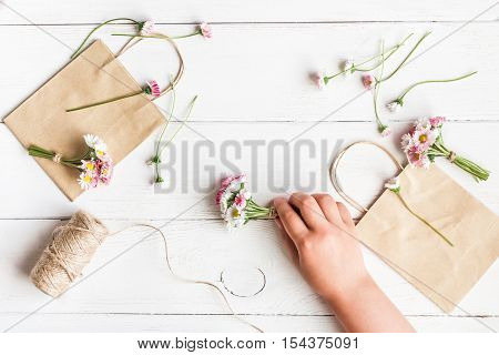 Workspace with small bouquets of daisy flowers paper bags. Creation. Child's hand. Top view flat lay