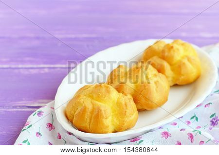 Tasty stuffed profiteroles. Homemade fresh profiteroles with with cream filling on a plate and on lilac wooden background. Closeup