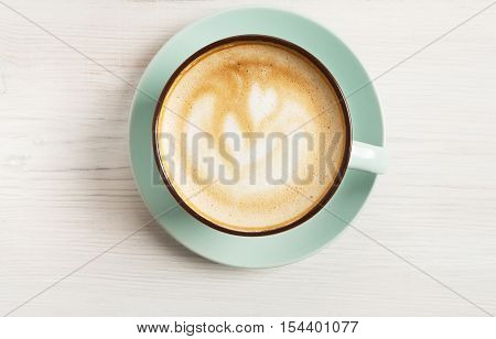 Cappuccino with frothy foam, blue coffee cup top view closeup on white wood background. Cafe and bar, barista art concept.