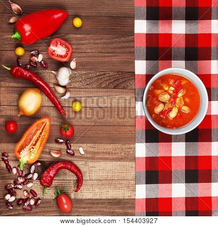 Soup Chili con carne on wooden background surrounded by vegetables.