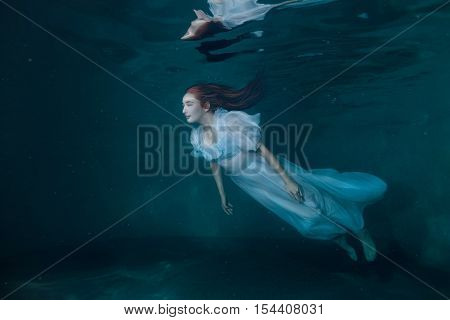 Fairy woman in a white dress under water it looks like a mermaid.