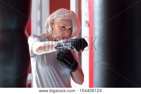 Boxing time. Serious pretty senior woman boxing punching bag while having workout in a gym.gray haired woman boxing in a gym.