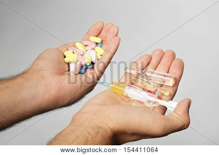 Male hands holding syringe and drugs on light background
