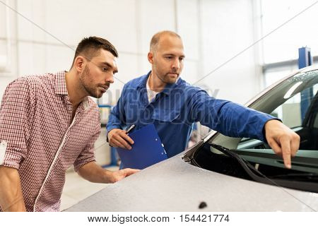auto service, repair, maintenance and people concept - mechanic checking windshield wiper and man or owner at car shop