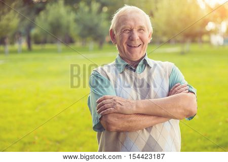 Senior man laughing. Person with crossed arms outdoor. The sense of joke. Wittiness and humor.