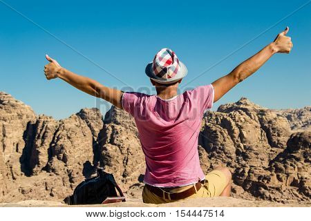 Photo of the Self-satisfied man in hat on top mountain with thumbs up. Do not give up motivation concept. Happy hiker winning reaching life goal success freedom and achievement.