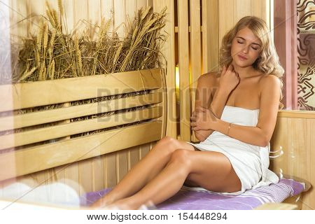 Young beautiful woman relaxing in the Finnish sauna wrapped in towel