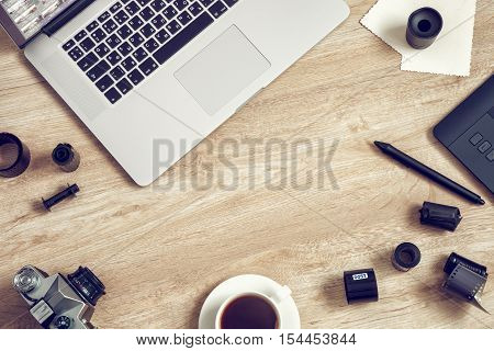 Work space for freelancer photographer retoucher designer: laptop retro camera film rolls digital tablet and coffee cup. Retro toned photo.