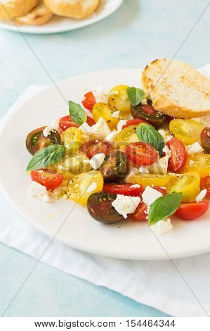 Summer heirloom tomato salad with fresh feta cheese on white plate on blue background selective focus vertical